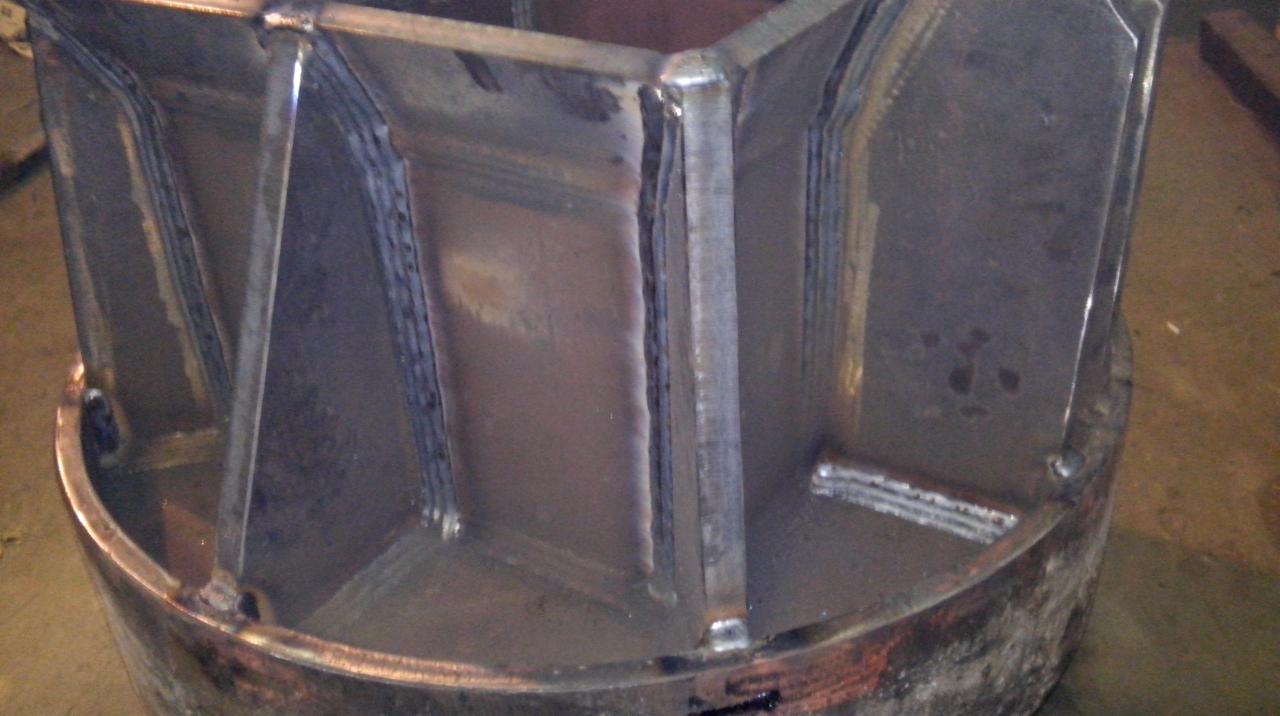 Wewnętrzny widok metalowej konstrukcji cylindrycznej z przyspawanymi wzmocnieniami, widoczne ślady po spawaniu i obróbce metalu.