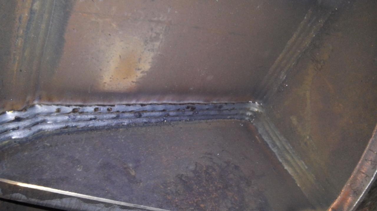 Wnętrze metalowej konstrukcji z widocznym, świeżym spawem, charakteryzującym się nierówną linią i widocznymi punktami spawania.