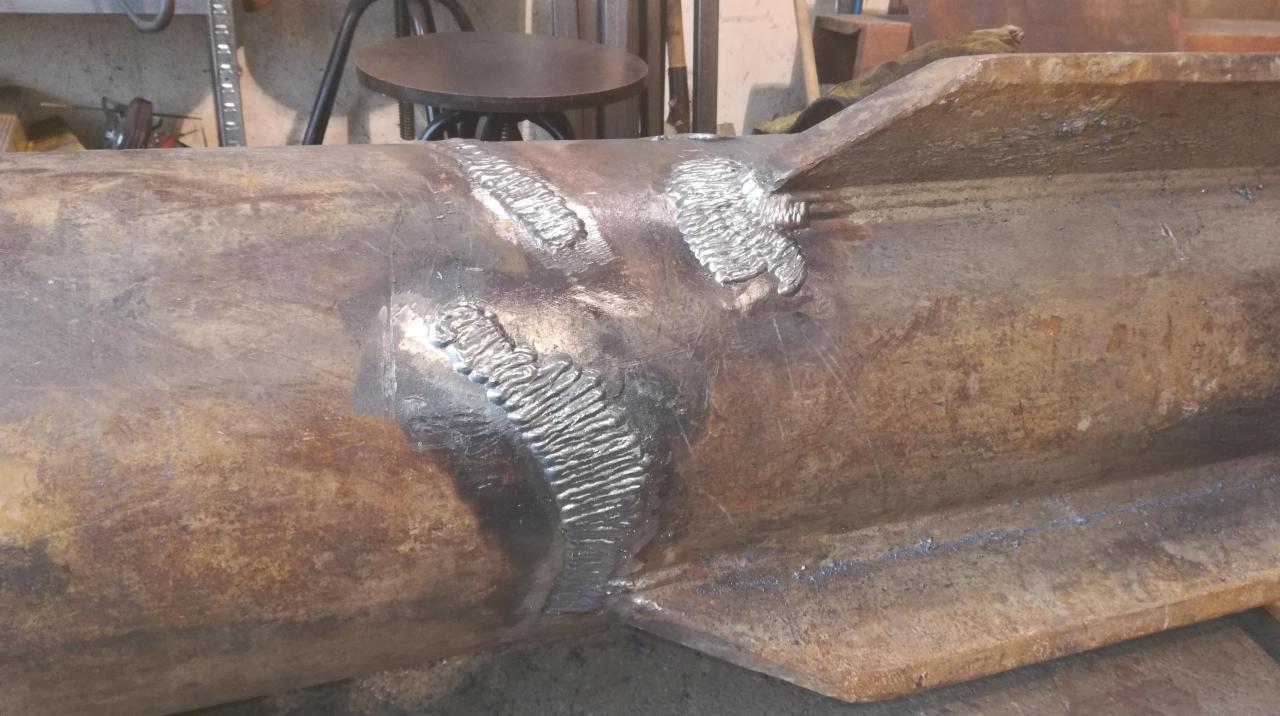 Spoina na zardzewiałym profilu stalowym z wyraźnymi śladami spawania, widoczne nierówności i charakterystyczny wzór na spoinie.