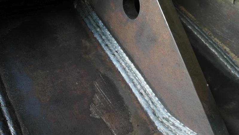 Spoina na grubym elemencie metalowym, widoczne ślady po spawaniu, nierówna powierzchnia metalu.