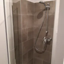 Nowoczesna kabina prysznicowa z przesuwnymi drzwiami, brązowe płytki na ścianach, chromowana bateria i słuchawka prysznicowa.