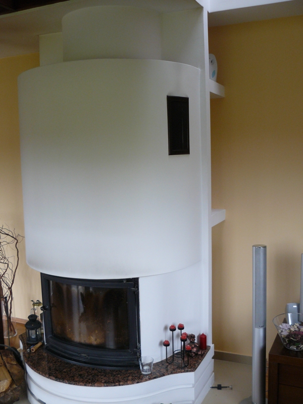 Nowoczesny, biały kominek z czarnym wkładem, wykończony brązowym blatem z granitu, otoczony dekoracjami, takimi jak świeczniki i szklanka.