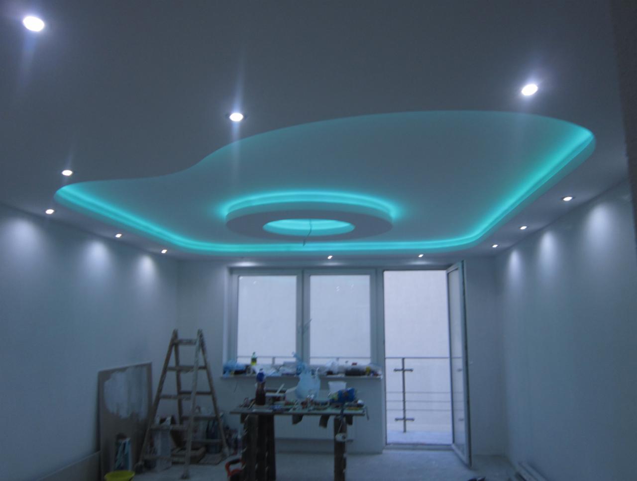 Nowoczesny sufit podwieszany z oświetleniem LED w kolorze turkusowym, widoczne narzędzia i drabina w pomieszczeniu w trakcie prac wykończeniowych.