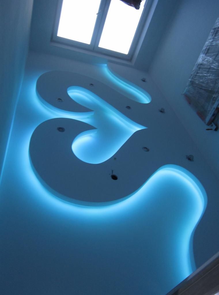 Nowoczesny sufit podwieszany z dekoracyjnym oświetleniem LED w Bytomiu, widok z dołu, z oknem dachowym w tle.