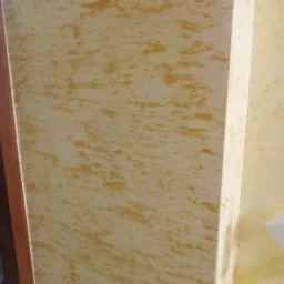 Ściana z efektem dekoracyjnym w odcieniach beżu i brązu, imitująca przecierkę, widoczny narożnik ściany i fragment sąsiedniej powierzchni.