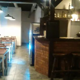 Wnętrze lokalu gastronomicznego z rzędami stolik&oacute;w i krzeseł, bar z cegły i chłodziarka Pepsi w tle, oświetlenie lampami wiszącymi.