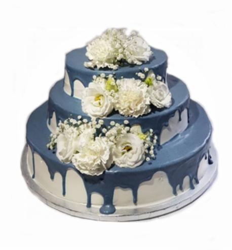 Trzypiętrowy tort z niebieskim lukrem spływającym po bokach i dekorowany białymi kwiatami.