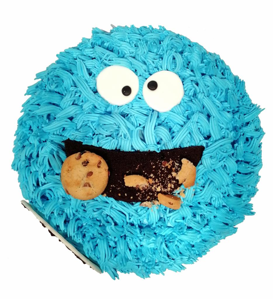 Tort w kształcie potwora ciasteczkowego z niebieskim kremem, dużymi oczami z lukru i ciasteczkami w ustach, widok z góry na białym tle.
