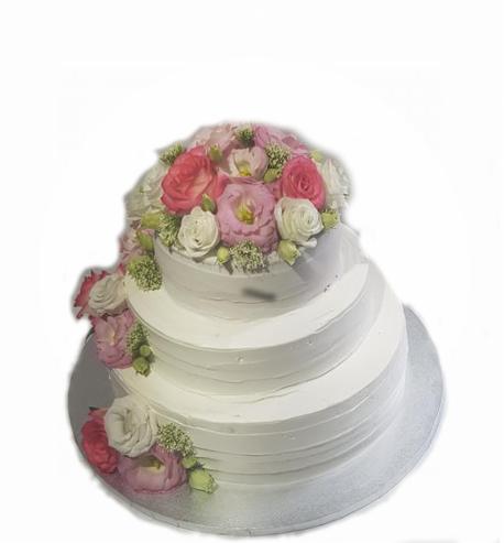 Trzypiętrowy tort weselny z białym kremem i dekoracją z różowych i białych róż oraz zielonych dodatków, umieszczony na srebrnej tacy.