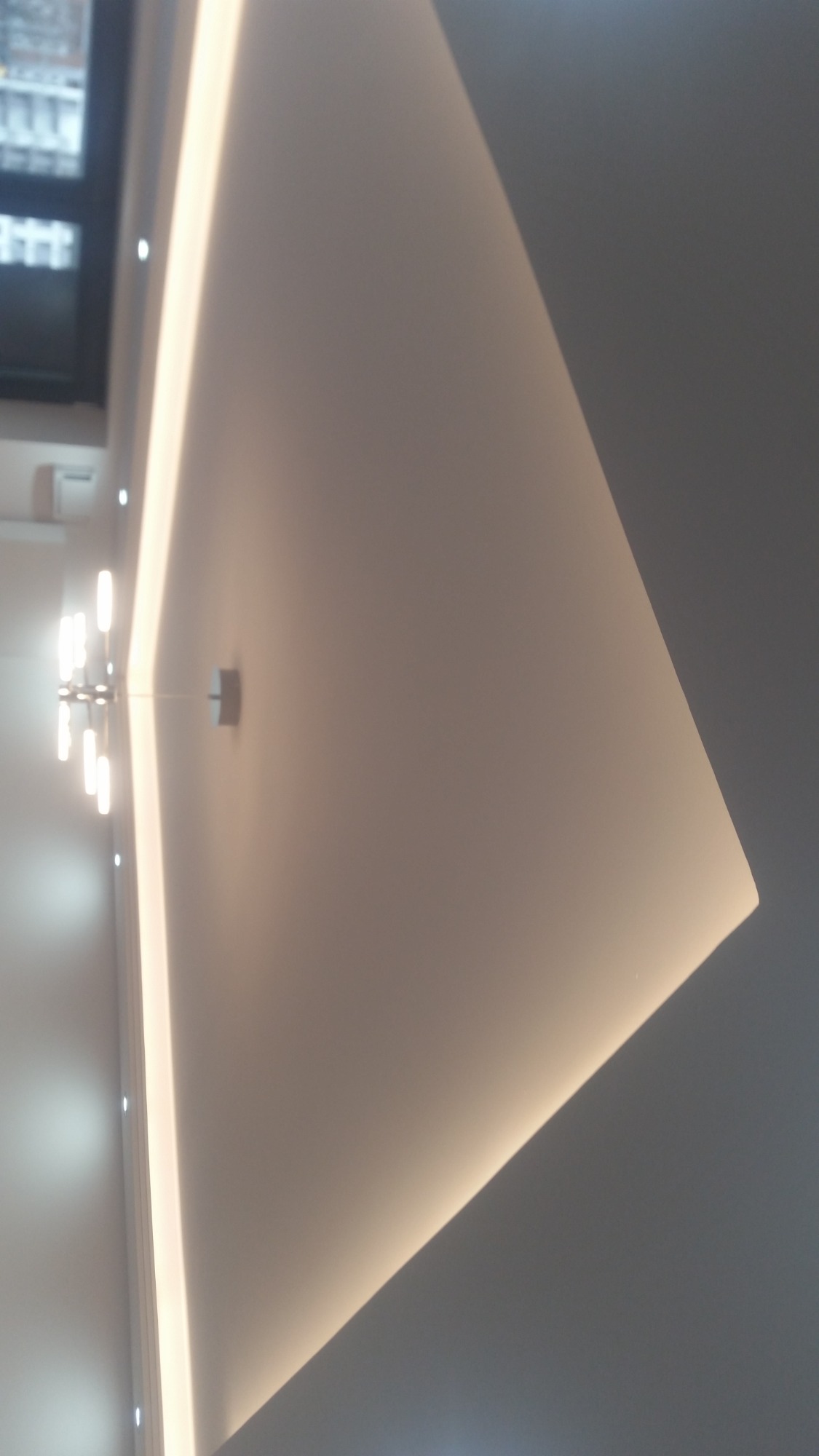 Nowoczesny sufit z oświetleniem LED wzdłuż krawędzi, widoczny fragment ściany z oświetleniem punktowym i okno w tle.