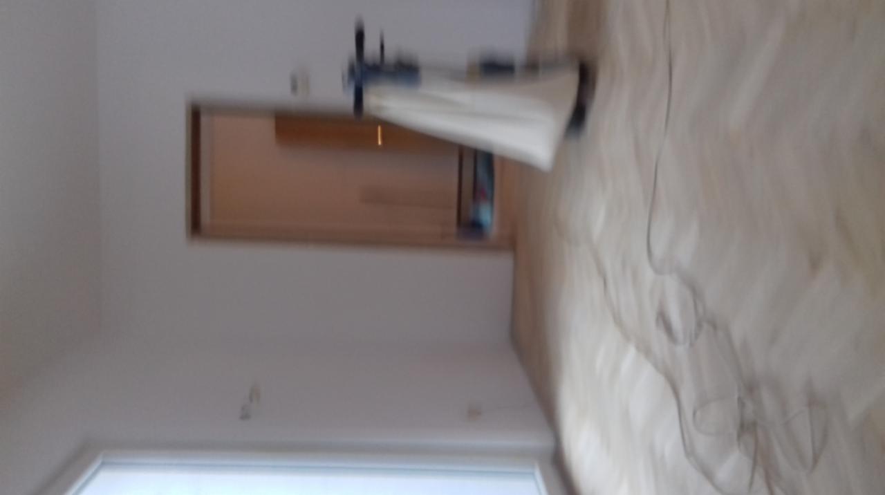 Pokój w trakcie malowania, widoczna maszyna do malowania natryskowego i częściowo pomalowane ściany na biało, podłoga parkiet. Zdjęcie rozmazane.