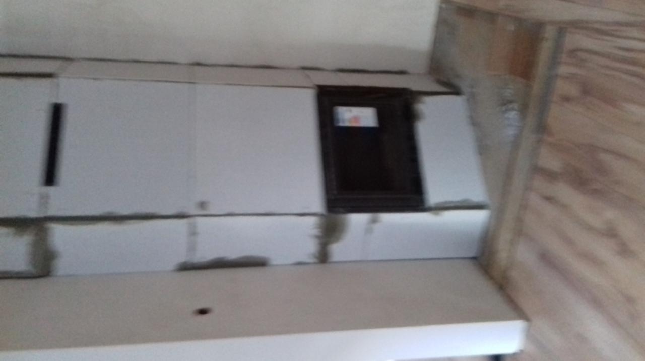 Wnętrze poddasza w trakcie ocieplania, widoczne białe płyty izolacyjne z szarymi spoinami, małe okno i fragment drewnianej boazerii.