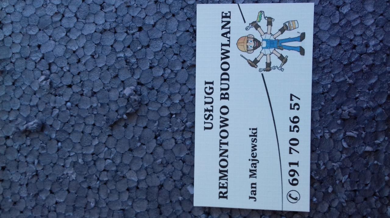 Wizytówka firmy budowlanej 'Usługi Remontowo Budowlane Jan Majewski' leżąca na fragmencie styropianu.