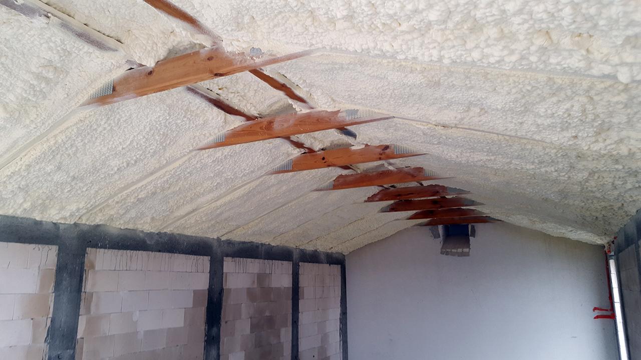 Poddasze z drewnianą konstrukcją pokryte grubą warstwą białej pianki PUR, widoczne fragmenty ściany z pustaków.