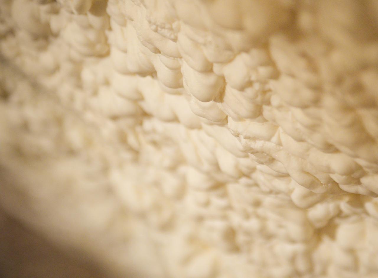 Nierówna, kremowa powierzchnia izolacyjna z pianki, zbliżenie na strukturę z widocznymi pęcherzykami powietrza.