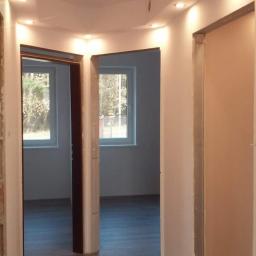 Usługi remontowo budowlane - Wnętrze mieszkania w trakcie prac wykończeniowych, widoczne osadzone ościeżnice drzwiowe, podłoga wyłożona panelami imitującymi drewno i zamontowane oświetlenie sufitowe punktowe.