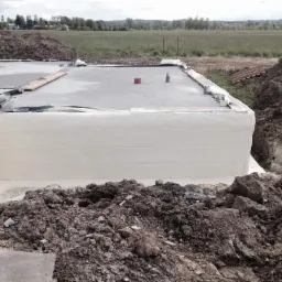 Fundament budynku po izolacji natryskowej, widoczne ślady ziemi na piance, w tle zielone pole i drzewa.