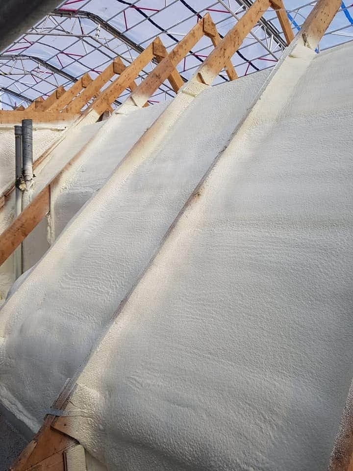 Skośny dach od wewnątrz, pokryty grubą warstwą białej pianki izolacyjnej, widoczne drewniane krokwie i konstrukcja dachu