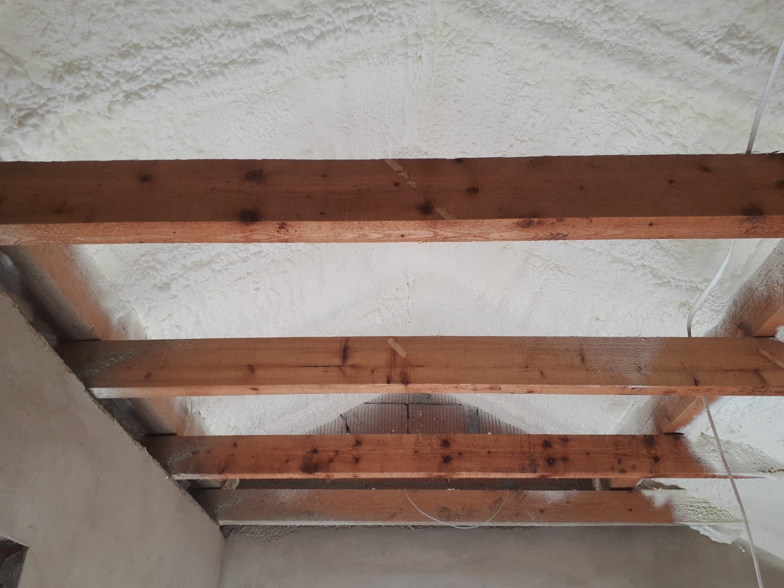 Biała pianka izolacyjna wypełniająca przestrzeń między drewnianymi belkami stropu w trakcie aplikacji.