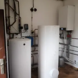 Dwa białe zbiorniki akumulacyjne Viessmann w pomieszczeniu kotłowni, widoczne rury miedziane i instalacja grzewcza na ścianie, brązowe płytki na podłodze.