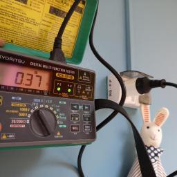 Voltage Adam Kwaśniewski - Pomiar rezystancji izolacji w gniazdku elektrycznym za pomocą cyfrowego multimetru Kyortisu KWE 6010B, widoczny kabel i wtyczka, w tle pluszowy królik.