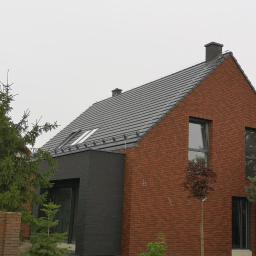 Voltage Adam Kwaśniewski - Nowoczesny dom jednorodzinny z czerwoną ceglaną elewacją i grafitowym dachem z zamontowanymi oknami dachowymi oraz instalacją odgromową.