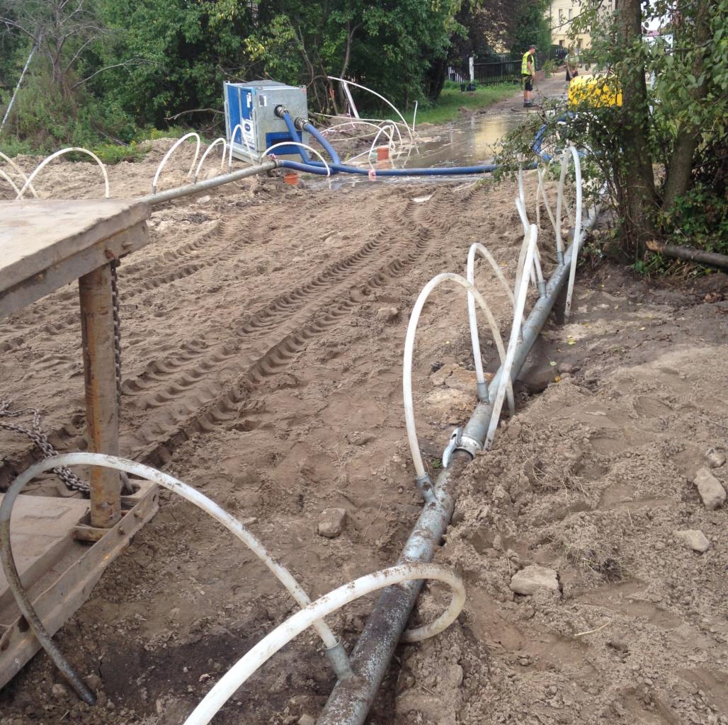 System rur z podłączonymi wężykami i agregatem na grząskim terenie z koleinami, prawdopodobnie w trakcie osuszania terenu.