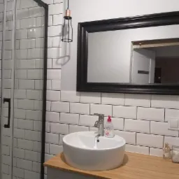 Wykończona łazienka z kabiną prysznicową z czarnymi ramami, białą umywalką nablatową na drewnianym blacie, białymi płytkami typu metro i czarnym lustrem.