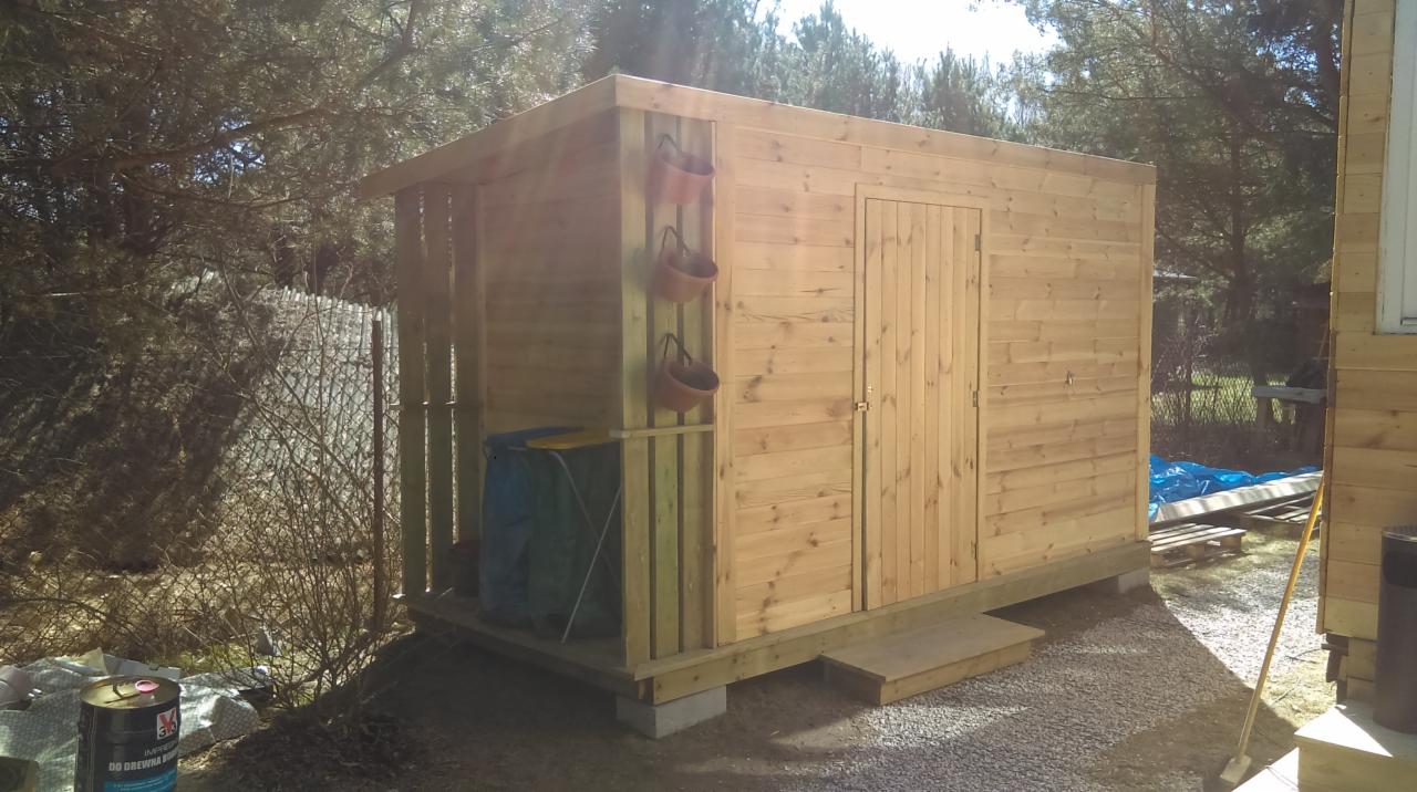 Świeżo zbudowana drewniana szopa z zamontowanymi doniczkami, widoczny pojemnik na narzędzia i puszka impregnatu do drewna.