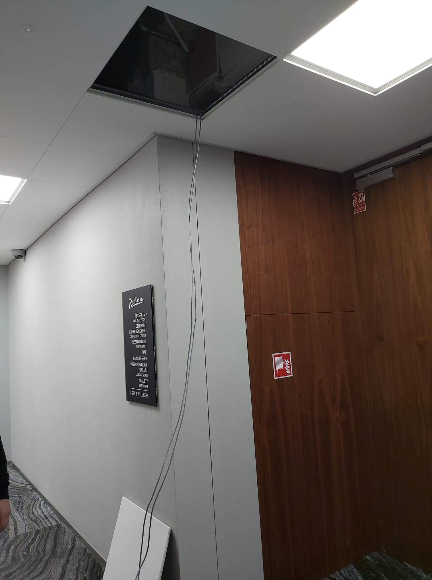 Otwór w suficie podwieszanym z widocznymi kablami w korytarzu hotelu Radisson.