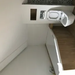 Nowoczesna toaleta podwieszana z widocznym panelem sterującym, umywalką w zabudowie i drewnopodobnymi płytkami na podłodze oraz dekoracyjnymi płytkami nad zabudową.