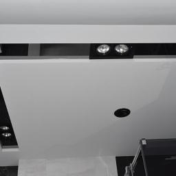 New Home KT Usługi remontowo-wykończeniowe - Nowoczesny sufit podwieszany z oświetleniem punktowym LED w czarnych oprawach, widoczne elementy konstrukcyjne i otwór na dodatkowe oświetlenie.