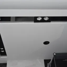 Nowoczesny sufit podwieszany z oświetleniem punktowym LED w czarnych oprawach, widoczne elementy konstrukcyjne i otwór na dodatkowe oświetlenie.