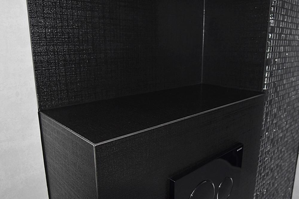 Czarna, wnęka w łazience w Szebniach, wykończona płytkami mozaikowymi i panelem z przyciskiem spłukującym, oświetlona z góry.