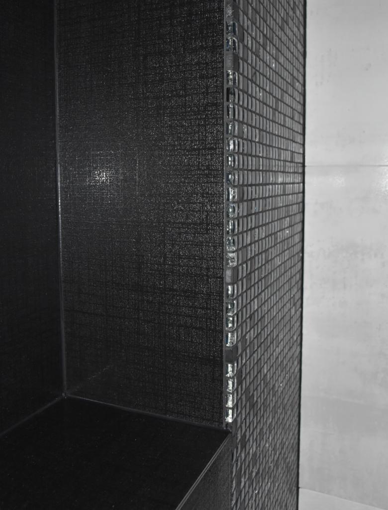 Półka wnękowa wykończona czarną mozaiką i płytkami imitującymi tkaninę, z błyszczącymi, szklanymi elementami dekoracyjnymi na krawędziach.