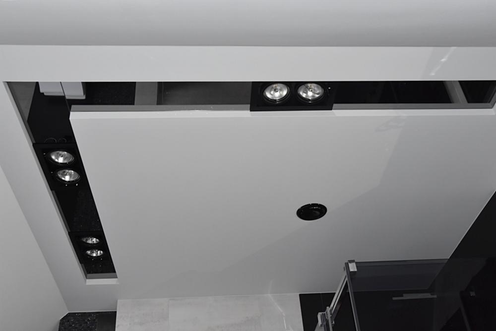 Nowoczesny sufit podwieszany z oświetleniem punktowym LED w czarnych oprawach, widoczne elementy konstrukcyjne i otwór na dodatkowe oświetlenie.