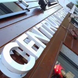 Montaż przestrzennego napisu 'CENTRUM PARKIET' na elewacji budynku z brązowego drewna. Widoczne kable i drabina.