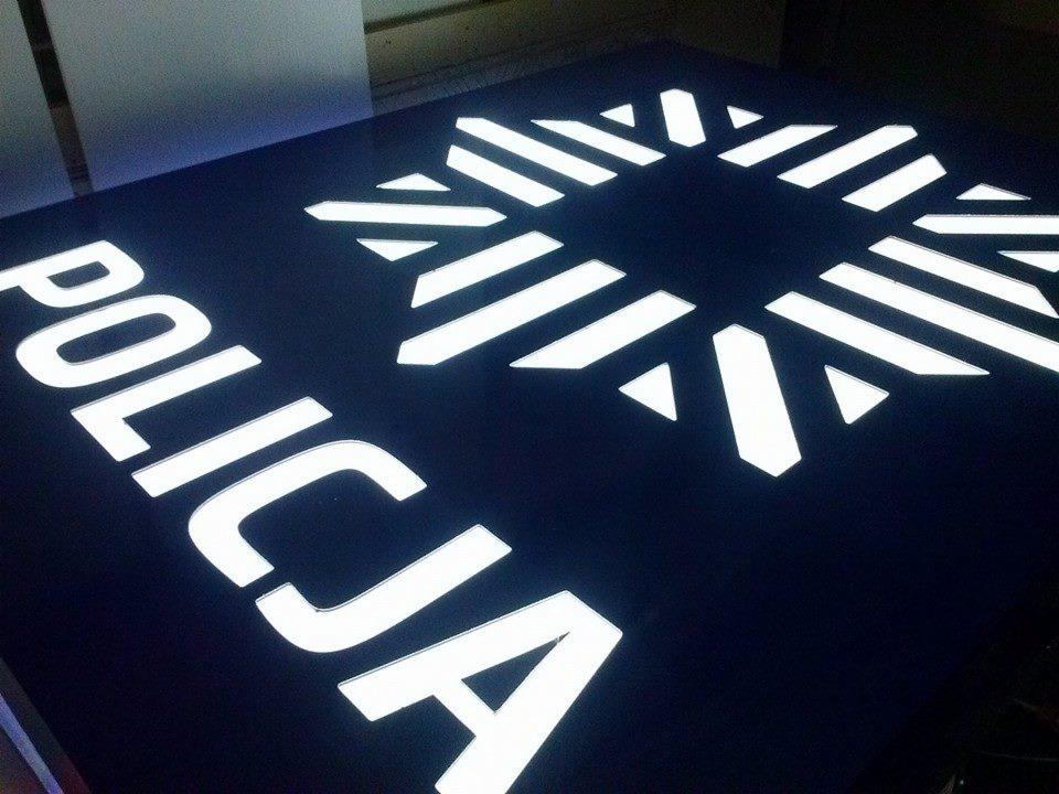 Podświetlany szyld z napisem 'POLICJA' i stylizowanym symbolem, wykonany na ciemnym tle.