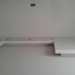 Minimalistyczne, białe wnętrze z podwieszanym sufitem w kształcie litery L, oświetleniem punktowym i wiszącą lampą z ażurowymi elementami, uzupełnione wiszącymi roślinami w górnym lewym rogu.