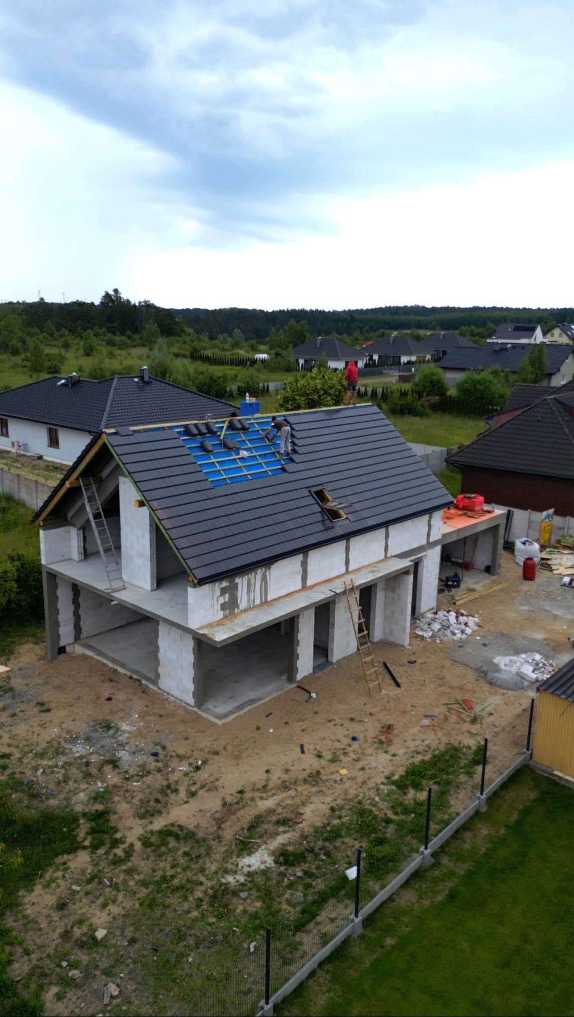 Montaż dachówki na nowym domu jednorodzinnym. Widoczne rusztowanie i dachówka w kolorze grafitowym. Prace dekarskie w toku, z bliska.