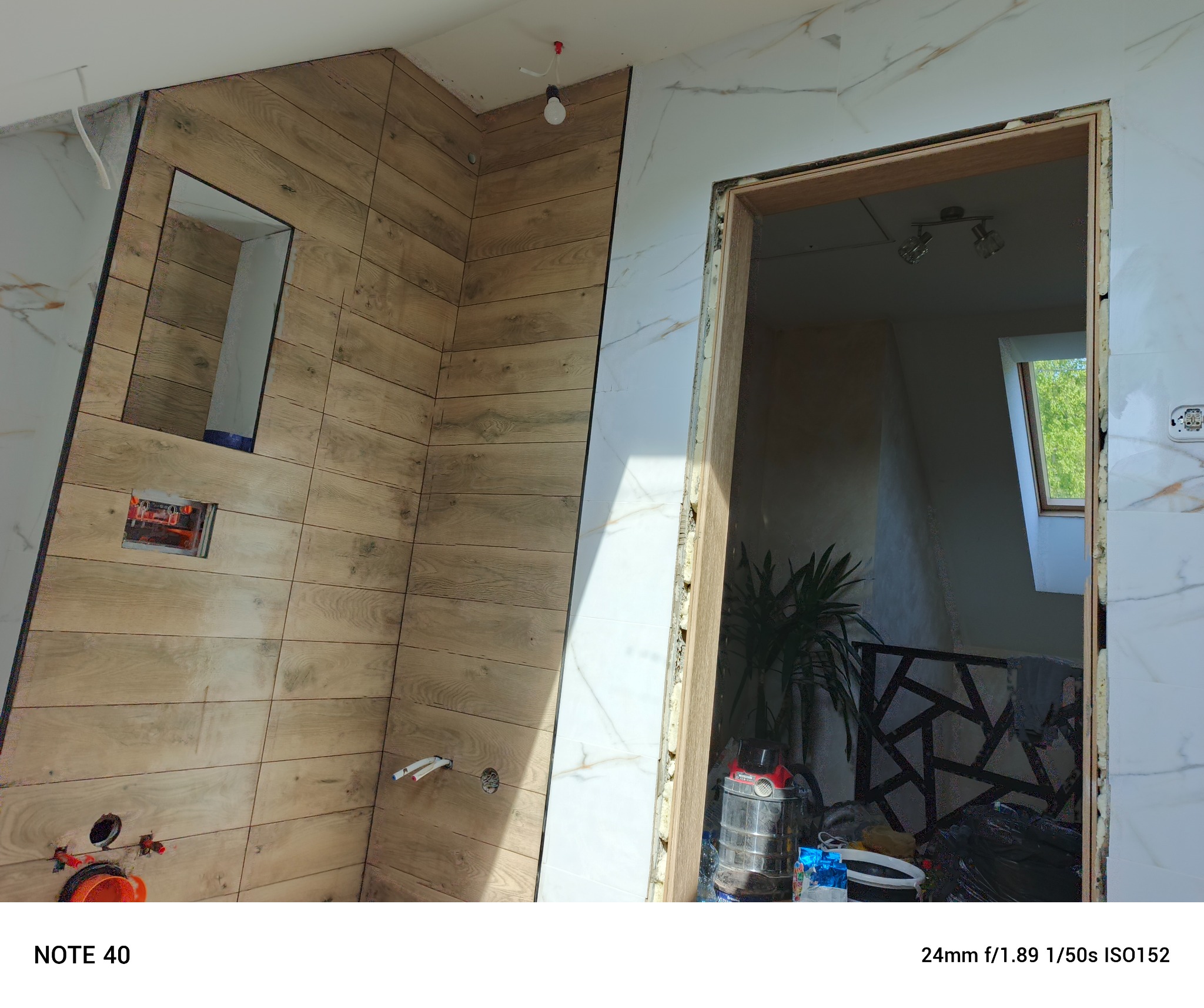 Wnętrze łazienki w trakcie wykończenia: drewnopodobne płytki, białe marmurowe płytki, surowa ościeżnica, instalacja sanitarna i elektryczna. Prace wykończeniowe.