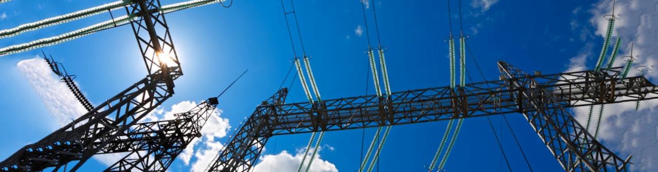 Słupy wysokiego napięcia z przewodami i izolatorami na tle błękitnego nieba z chmurami, widok z dołu.