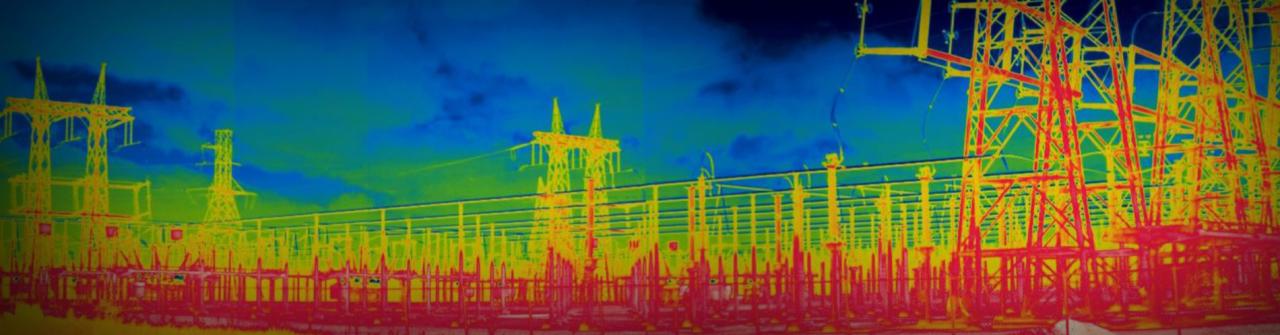 Termowizyjne ujęcie stacji transformatorowej z widocznymi wieżami i liniami wysokiego napięcia na tle błękitnego nieba.