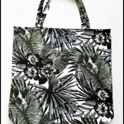 Torba bawełniana typu shopper z czarno-białym wzorem tropikalnych liści i kwiatów hibiskusa, widoczna na białym tle.