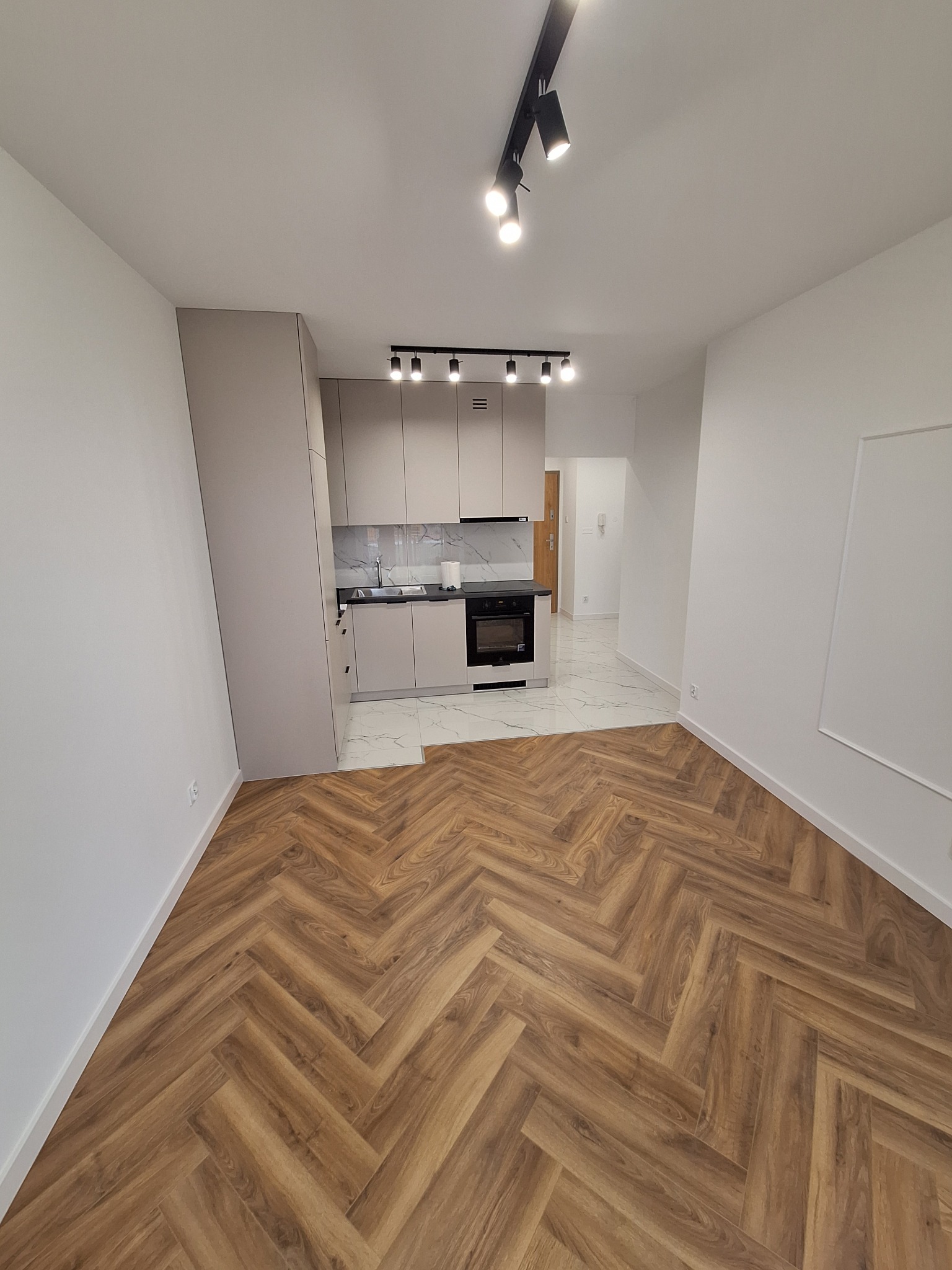 Jasne wnętrze po remoncie z drewnianą podłogą ułożoną w jodełkę i minimalistyczną zabudową kuchenną z marmurowym backsplashiem oraz oświetleniem punktowym.