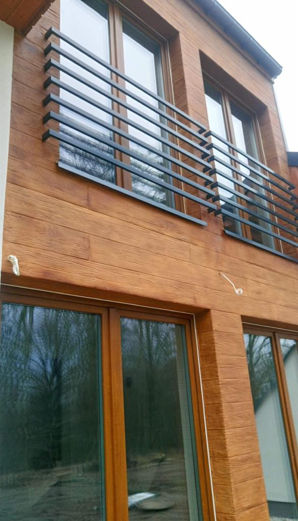 Dwukondygnacyjny budynek z elewacją imitującą drewno, z oknami w drewnianych ramach i metalowymi balustradami balkonowymi.