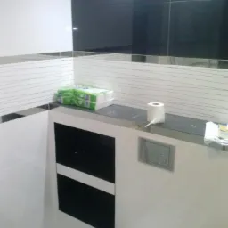 Nowoczesna łazienka z czarno-białymi płytkami, ukryta spłuczka WC, wnęka z półkami, rolka papieru toaletowego i paczka chusteczek na blacie.