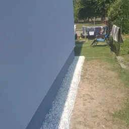 Świeżo pomalowana, jasnoszara ściana budynku z nowym obłożeniem z białego grysu przy fundamencie, widok z boku w słoneczny dzień.