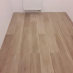 Ułożone panele podłogowe imitujące drewno w małym pomieszczeniu z grzejnikiem na ścianie.