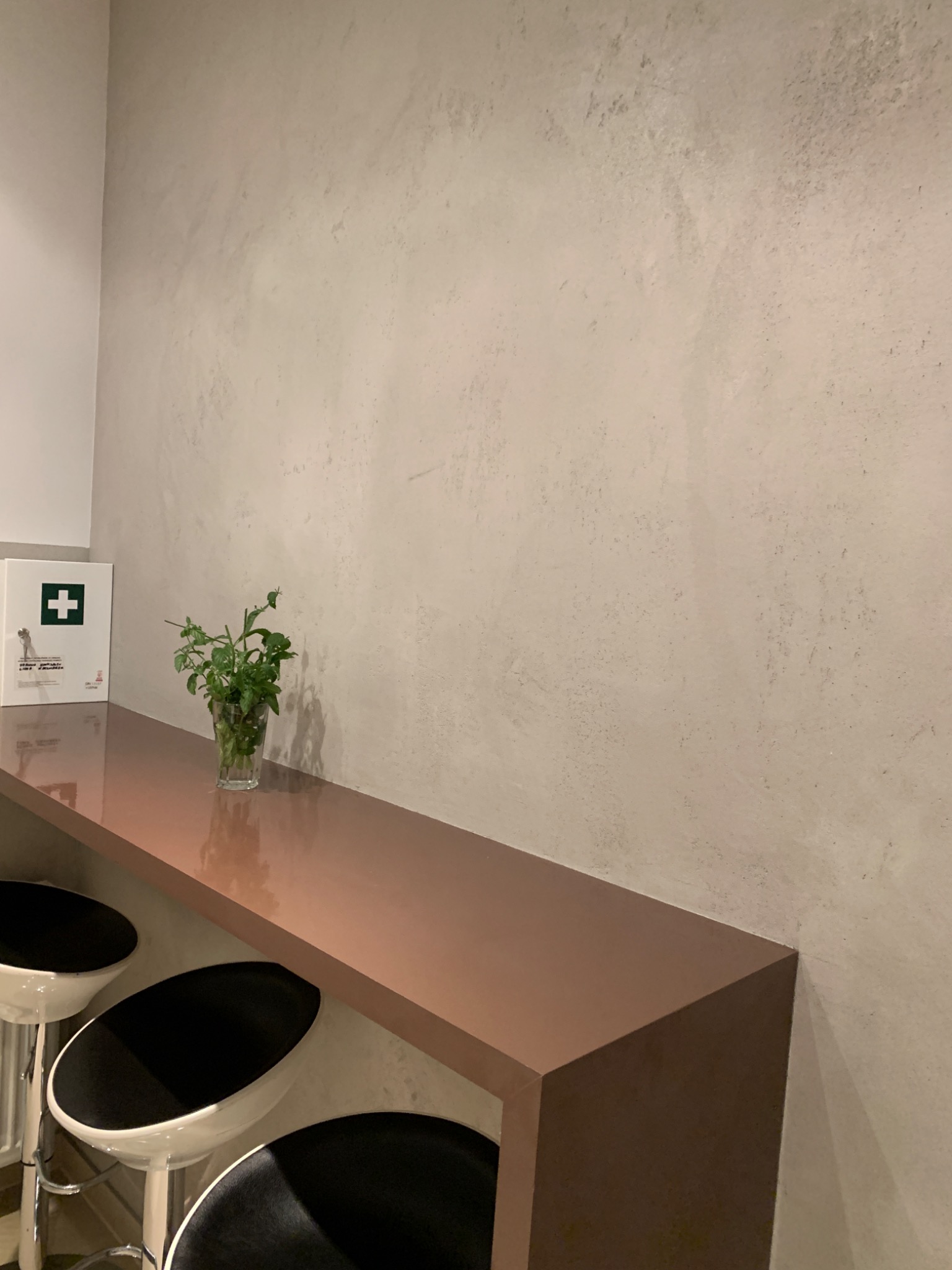 Ściana z efektem dekoracyjnym, bar z hokerami i roślina w szklance, obok apteczka.